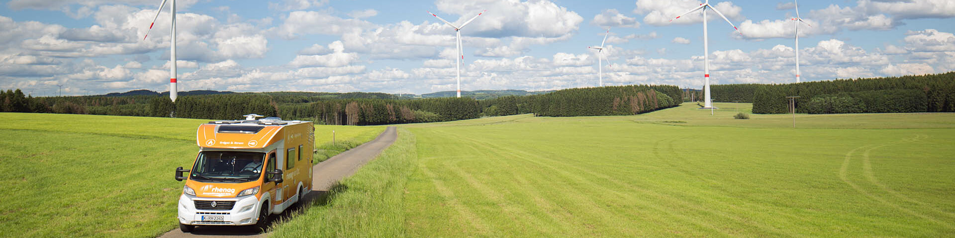 Rhenag Mobil auf Stasse zwischen Feldern, Windräder im Hitnergrund Rhenag Mobil auf Stasse zwischen Feldern, Windräder im Hitnergrund