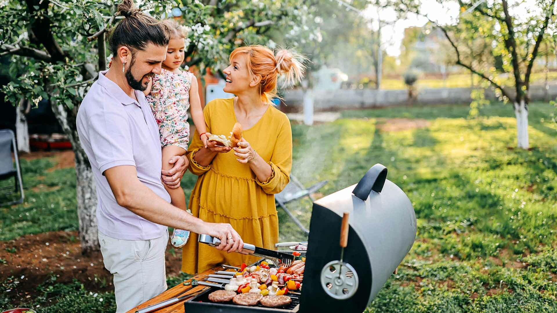 Grillen Junge Familie vor einem Grill im Garten