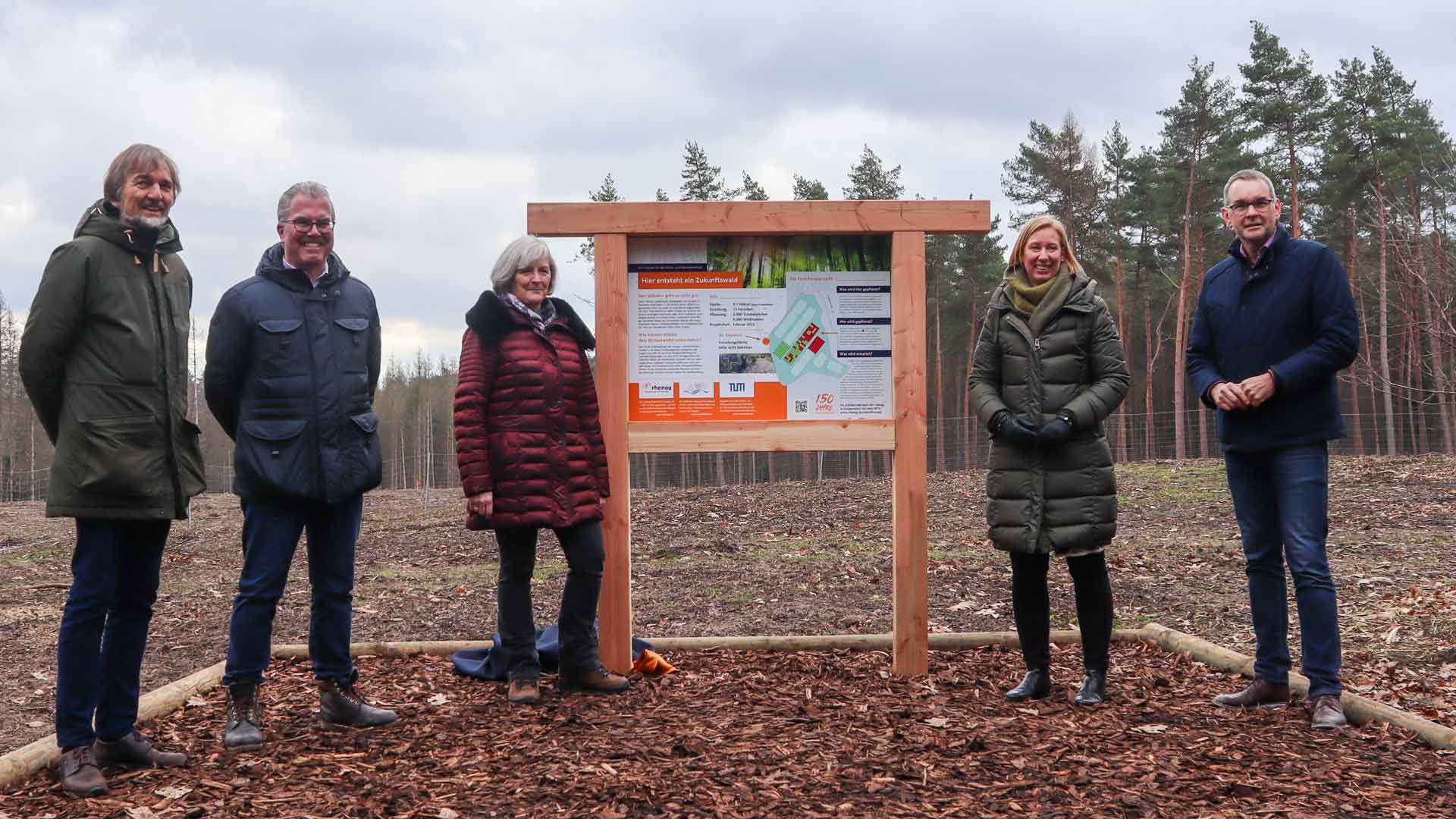 Zukunftswald Projektmitarbeiter stehen vor der Zukunftswald Erklärtafel.