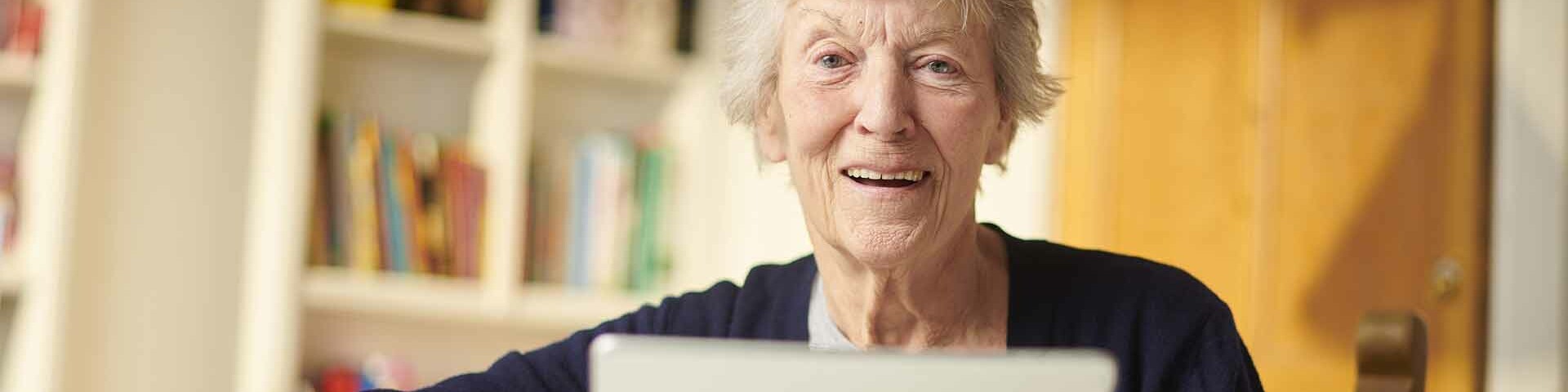 Tablets Ältere Frau mit kurzen Haaren hält in ihrem Zimmer ein Tablet in den Händen.