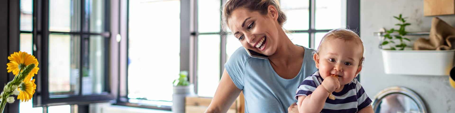 Haushalt Frau mit Kleinkind auf dem Arm steht telefonierend in der Küche.