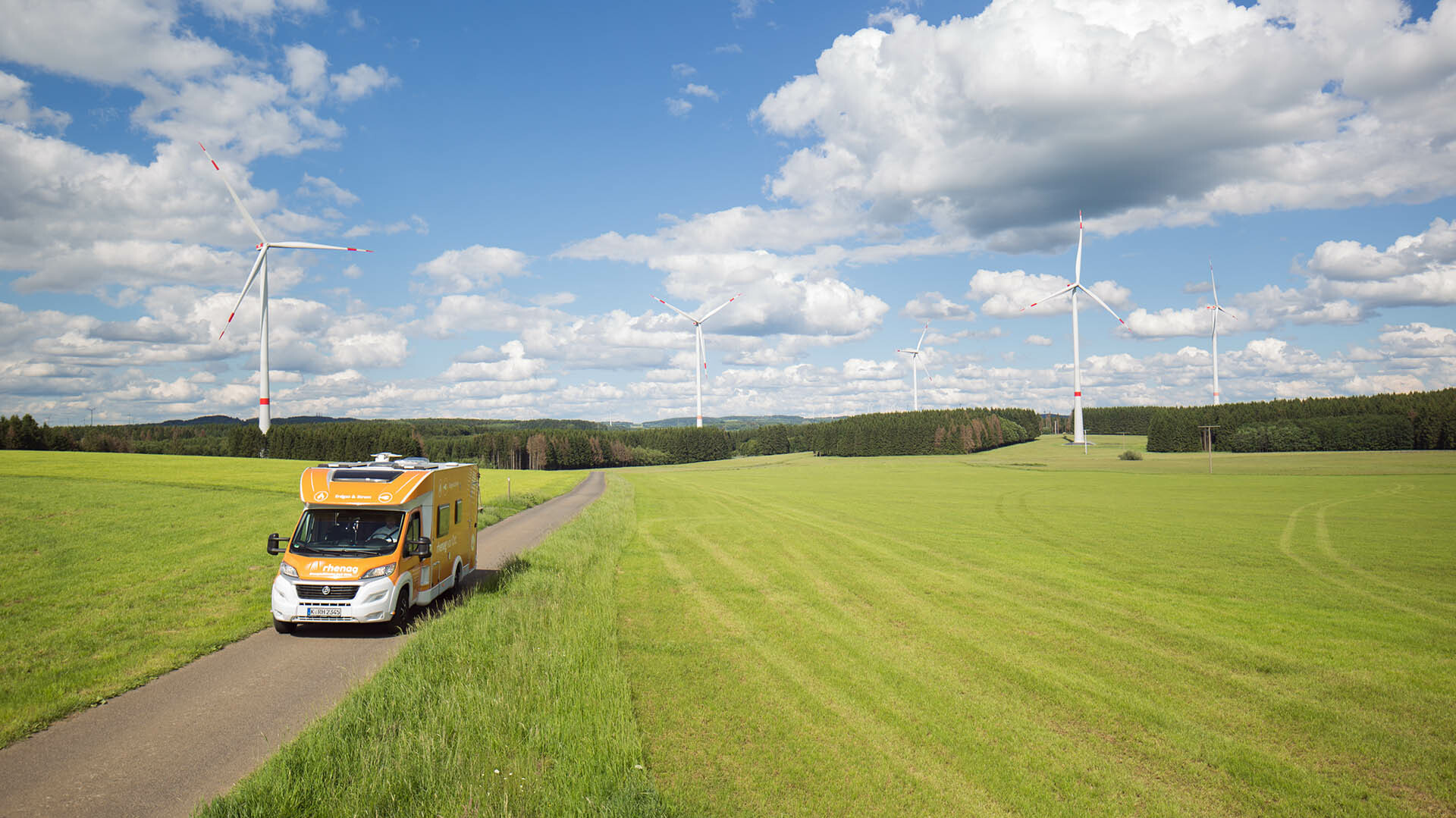 Rhenag Mobil auf Stasse zwischen Feldern, Windräder im Hitnergrund Rhenag Mobil auf Stasse zwischen Feldern, Windräder im Hitnergrund
