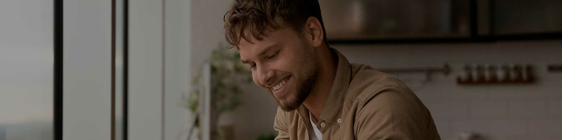 Kontakt Mann sitzt mit Laptop am Schreibtisch und lächelt.