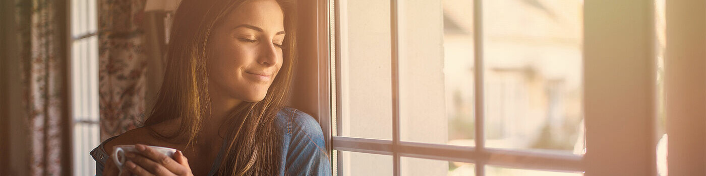Dunkelhaarige Frau mit Kaffetasse am Fenster stehend Dunkelhaarige Frau mit Kaffetasse am Fenster stehend