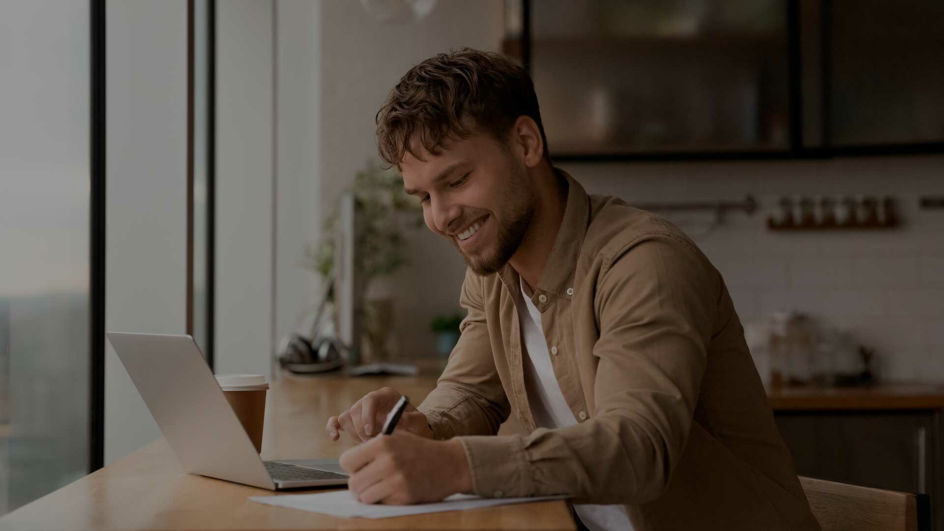 Kontakt Mann sitzt mit Laptop am Schreibtisch und lächelt.