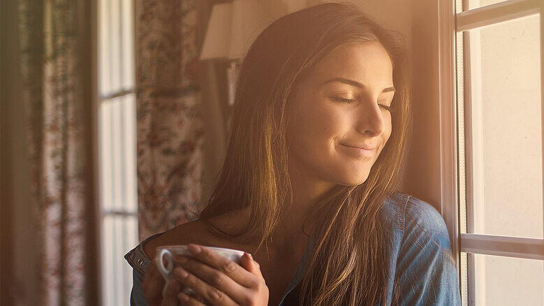Dunkelhaarige Frau mit Kaffetasse am Fenster stehend Dunkelhaarige Frau mit Kaffetasse am Fenster stehend